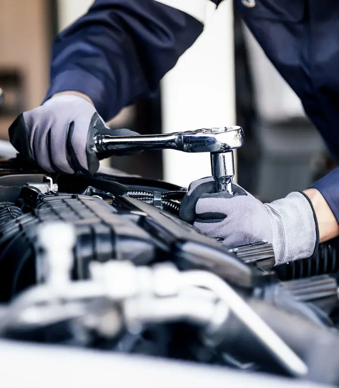 A Meineke technician in work gloves tightening a bolt under the hood of a car